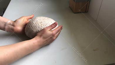 Woman shapes dough into round loaf and puts it into proving basket.