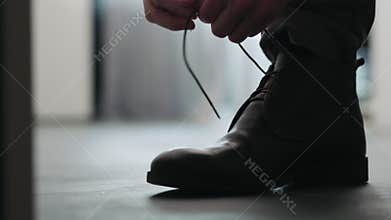 Young man put on his brown leather chukka boots indoor