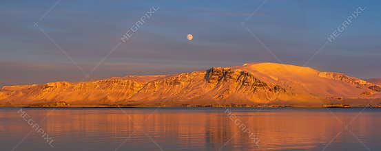 Sunset from the Reykjavik city waterfront promenade showing the full moon and the snow-capped and orange-lit islands of Engey and