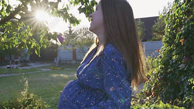 Beautiful pregnant woman enjoying fresh air at sunset rays on the backyard