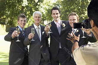 Man taking a picture of five men toasting with wine glasses at wedding party