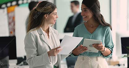 Two businesswomen lead conversation walk along hallway in modern office