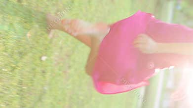 Vertical Video. Asian Girl Joyfully Races Barefoot Across the Grassy Terrain, Adorned in a Flowing Pink Gown.