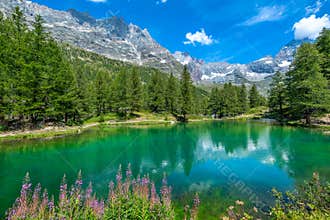 Small alpine lake and mountain ridge under blue sky in Italy