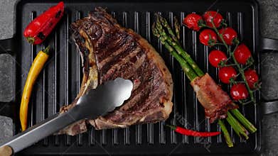 T- bone beef steak grill with vegetables on grill pan. Steak turning over on the grill. Top view. Slow motion
