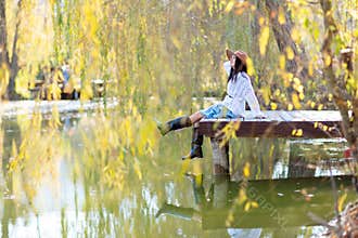 Autumn lake woman. She sits by a pond on a wooden pier in autumn and admires nature. The concept of tourism, weekends