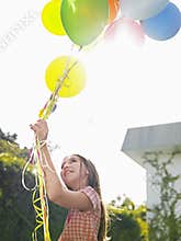 Young Girl Holding Up Balloons In Lawn