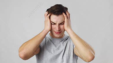 Young man suffering from headache attack, rubbing his aching head, grey studio background, slow motion