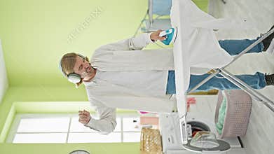 Smiling man ironing clothes in laundry room listening to headphones enjoying household chore