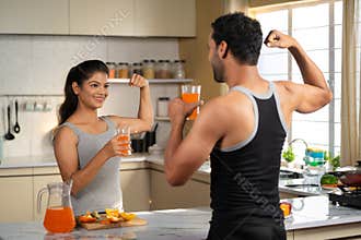 Joyful active fitness couples drinking nutritious orange juice after workout at kitchen by toasting - concept of healthy