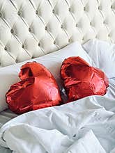 Two red heart-shaped balloons lie on a white bed in a retro bedroom. Wedding day or Valentine’s Day.