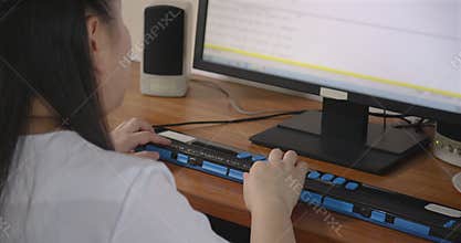 Rear view of woman with blindness disability using computer with braille display or braille terminal a technology assistive device