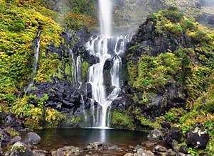 The Poco do Bacalhau waterfall in the Flores island of Azores. Green hills and fields. Sunny weather