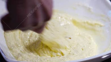 A woman&#x27;s hand mixes the dough with the added flour with a spoon.