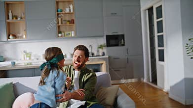 Cute girl catching father wearing blindfold home. Laughing daddy playing child
