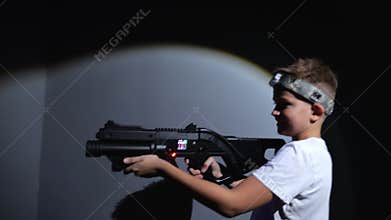 A happy teenage boy with a laser pistol is having fun in a dark laser tag arena.