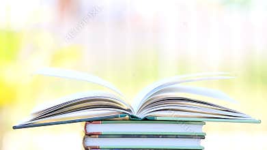 Open book in wind, green garden background.