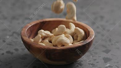 Slow motion dry cashew falling into olive bowl on terrazzo countertop