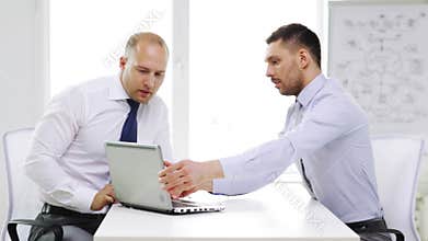 Two smiling businessmen with laptop in office