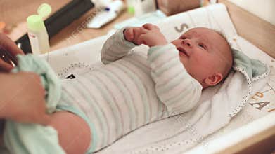 Woman changing diapers for her infant baby son laying on the table, smiling happily as she plays with him