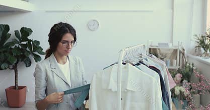 Young businesswoman organizing new female clothing collection on hangers.