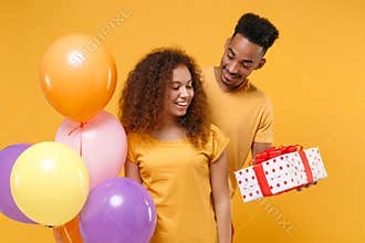 Pretty young friends couple african american guy girl isolated on yellow background. Birthday holiday party concept