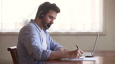 Skype teacher wearing headset looking at laptop screen making notes