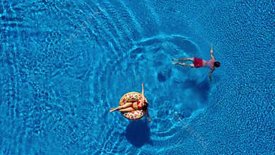 Aerial view of man dives into the the pool while girl is lying on a donut pool float