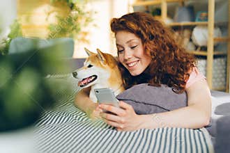 Joyful girl taking picture with shiba inu dog using smartphone to take selfie