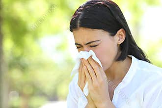 Ill woman sneezing covering mouth with a wipe in a park