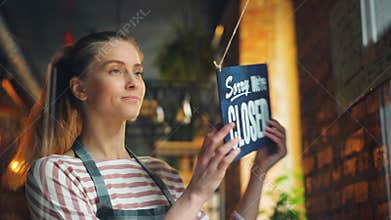 Young woman opening cafe in morning hanging we are open sign on front door