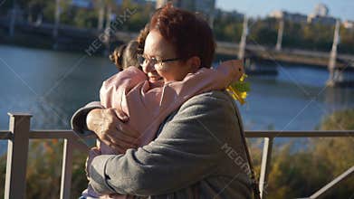 Granddaughter with a bouquet of yellow autumn leaves ran up to her grandmother and hugging her in a Park by the river.