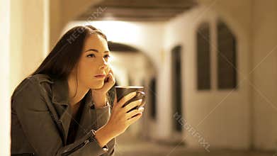 Pensive woman drinking coffee in the night