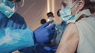 Caucasian senior woman having virus vaccine injection by medical nurse at hospital for coronavirus covid-19 immunization