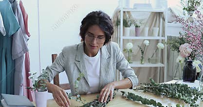 Young designer or florist making flower arrangement sitting at desk