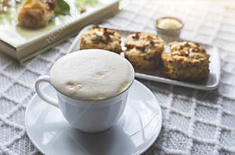 Home made cup of latte coffee beans with blurry cheese scones and summer book on coffee table with morning light or Cozy scene of