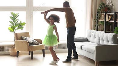 Happy african dad dancing with child daughter in living room