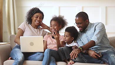 Happy african parents and children using devices together on sofa