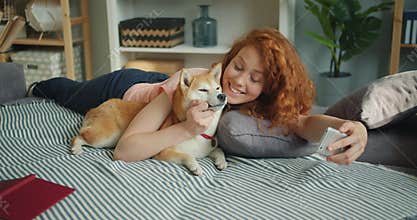 Teenage girl taking selfie with dog kissing pet using smartphone camera at home