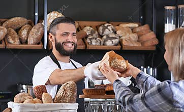 Young man giving fresh bread to woman in bakery
