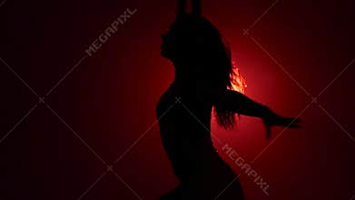 Silhouette aerialist girl doing acrobatic and flexible tricks on red aerial silks tissues on red background. Slow motion