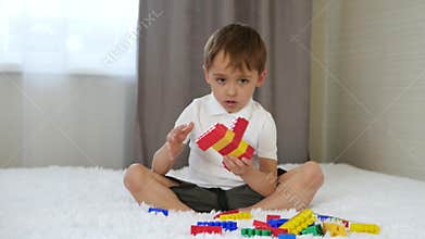 The child builds from colored blocks sitting on the bed in the room. Baby and toys.