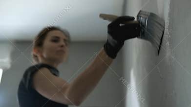 Woman is painting wall to grey colour