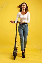 Young beautiful girl with electric scooter. Isolated on yellow background. Technology and freedom of movement.