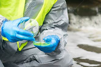 Against the background of the suit, the hands of the scientist in protective gloves, close the Petri dish with biomaterials