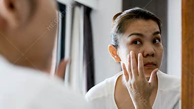 Middle aged asian woman looking at wrinkles and her facial problem in the mirror