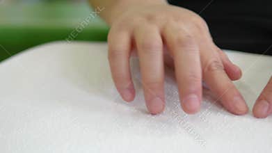 Close-up hand of person woman with blindness disability moving fingers reading Braille book studying in creative library. Braille