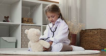 Engaged cute preschool girl in oversized white coat examining toy