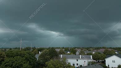 Stormy clouds forming on gloomy sky before heavy rainfall and lightning over suburban town city. Drone view