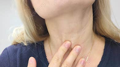Blonde middle-aged blonde European woman looks closely at the skin on her neck